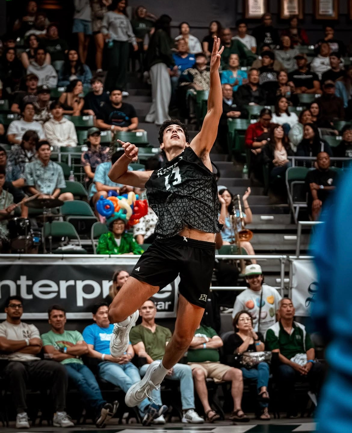 A volleyball player jumps to spike the ball in a crowded arena.